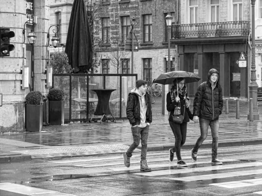 3 college students walking in  the rain. One holding a best college umbrella!