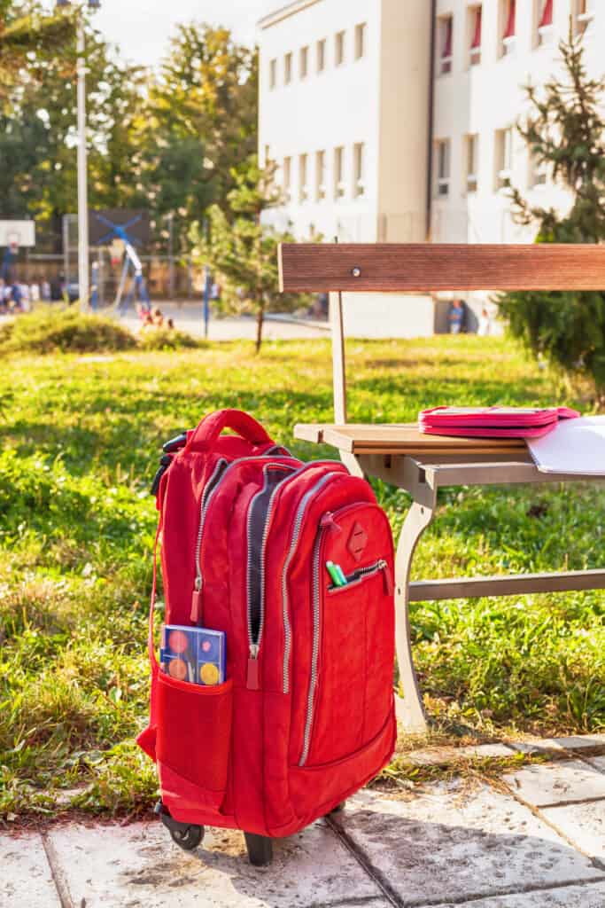 Red rolling backpack for students by a bench