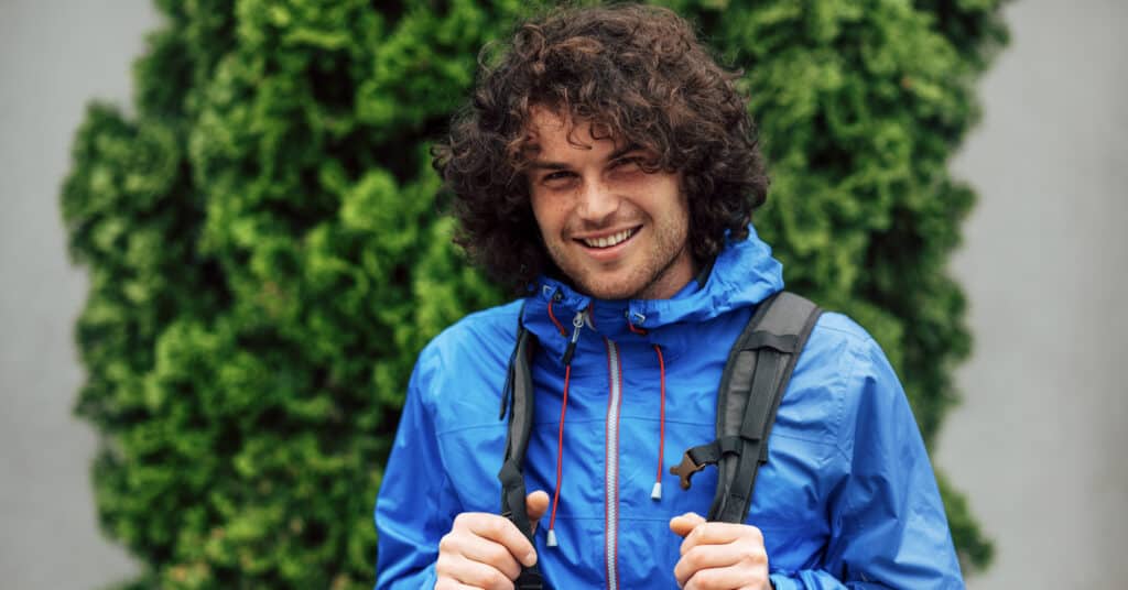 guy with curly hair and a blue raincoat carrying a waterproof backpack for college
